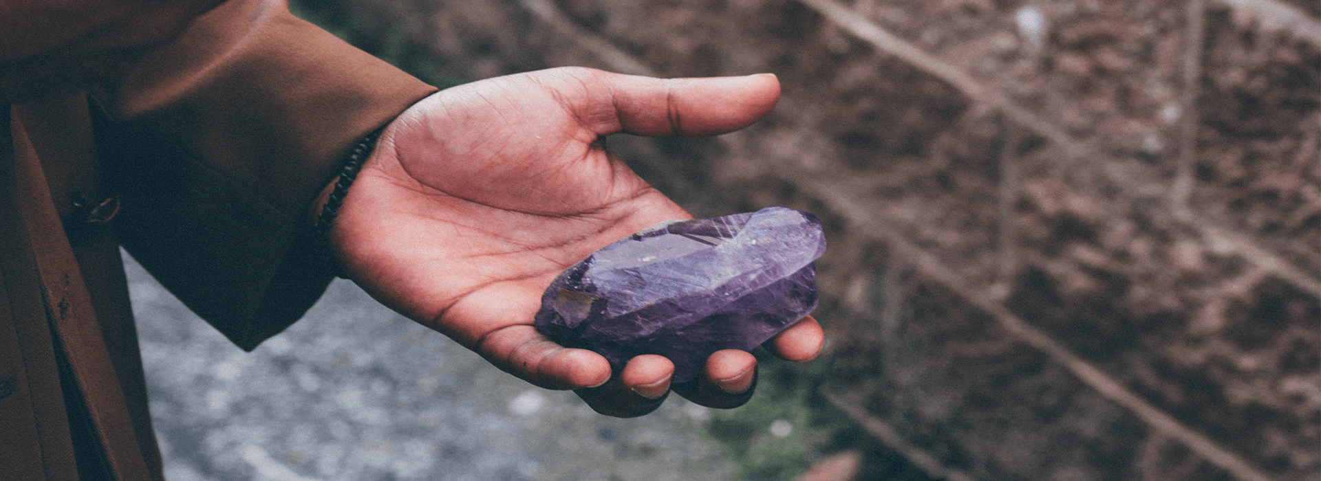 A large, rough purple amethyst crystal held in a hand to illustrate the collector and buyer career path.