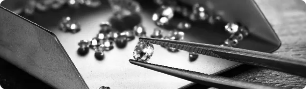 A professional black and white banner featuring a gemologist's tweezers precisely holding a brilliant-cut diamond over a tray of loose stones, symbolizing SGL's expert grading standards and attention to detail.